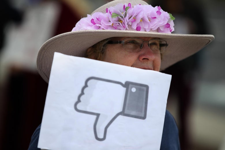 Woman holds a sign with the Facebook thumbs down symbol